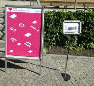 Pink poster of the soap! conference with another small sign showing arrow pointing to the right