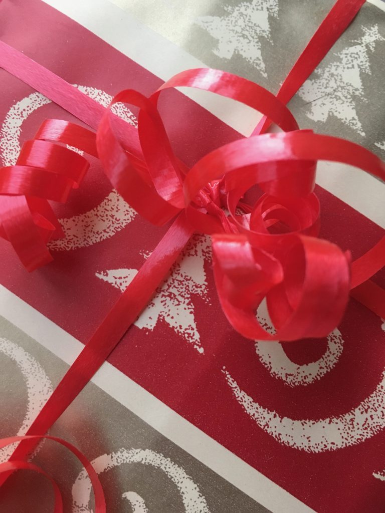 Close-up of red and gold striped wrapping paper tied with thin, curled, red ribbon